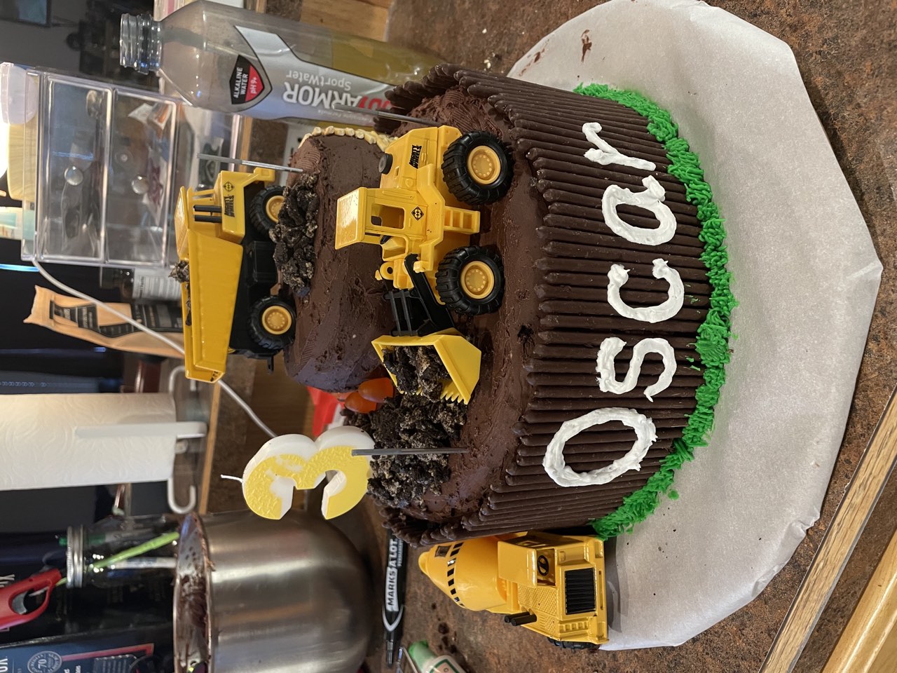Construction themed chocolate birthday cake with toy trucks and a number three candle