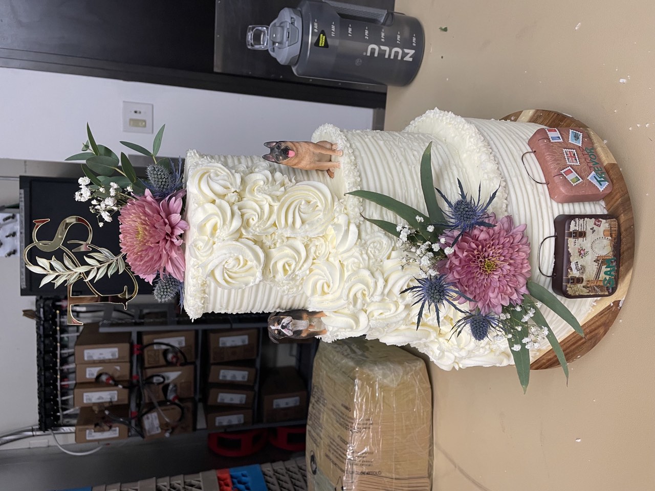 Two-tier buttercream wedding cake with floral accents and custom travel details